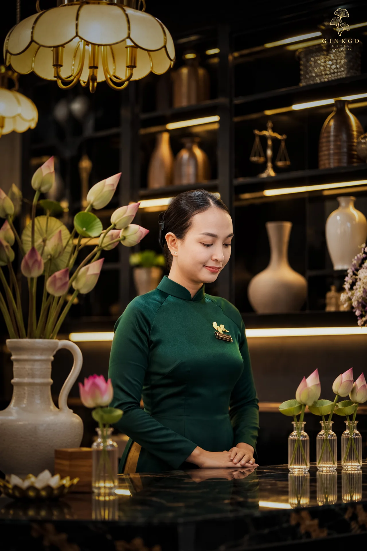 Lễ tân Ginkgo trong áo dài xanh bên quầy hoa sen